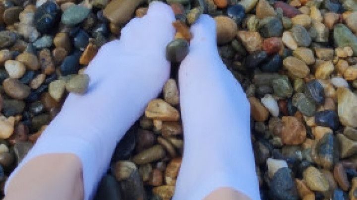 I play with my feet in white socks with pebbles on the beach