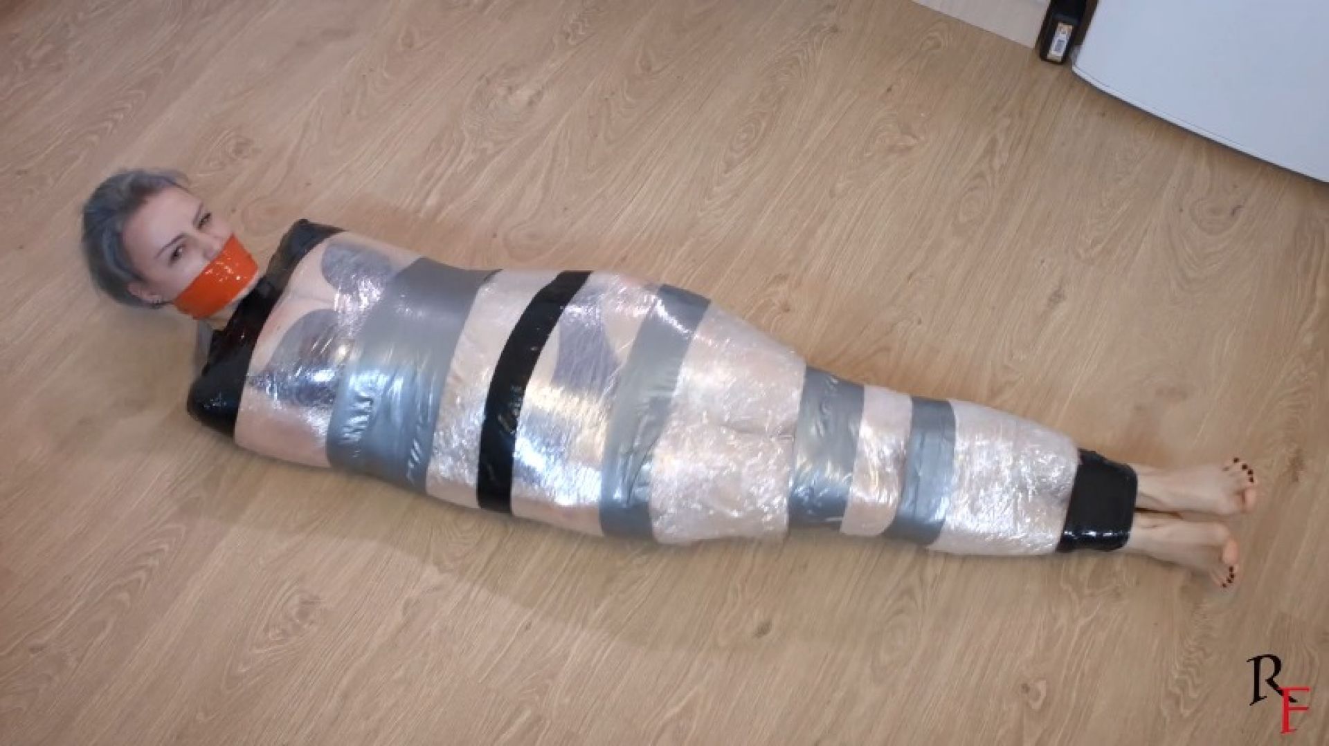 Barefoot Astrid is tightly wrapped with film and tape