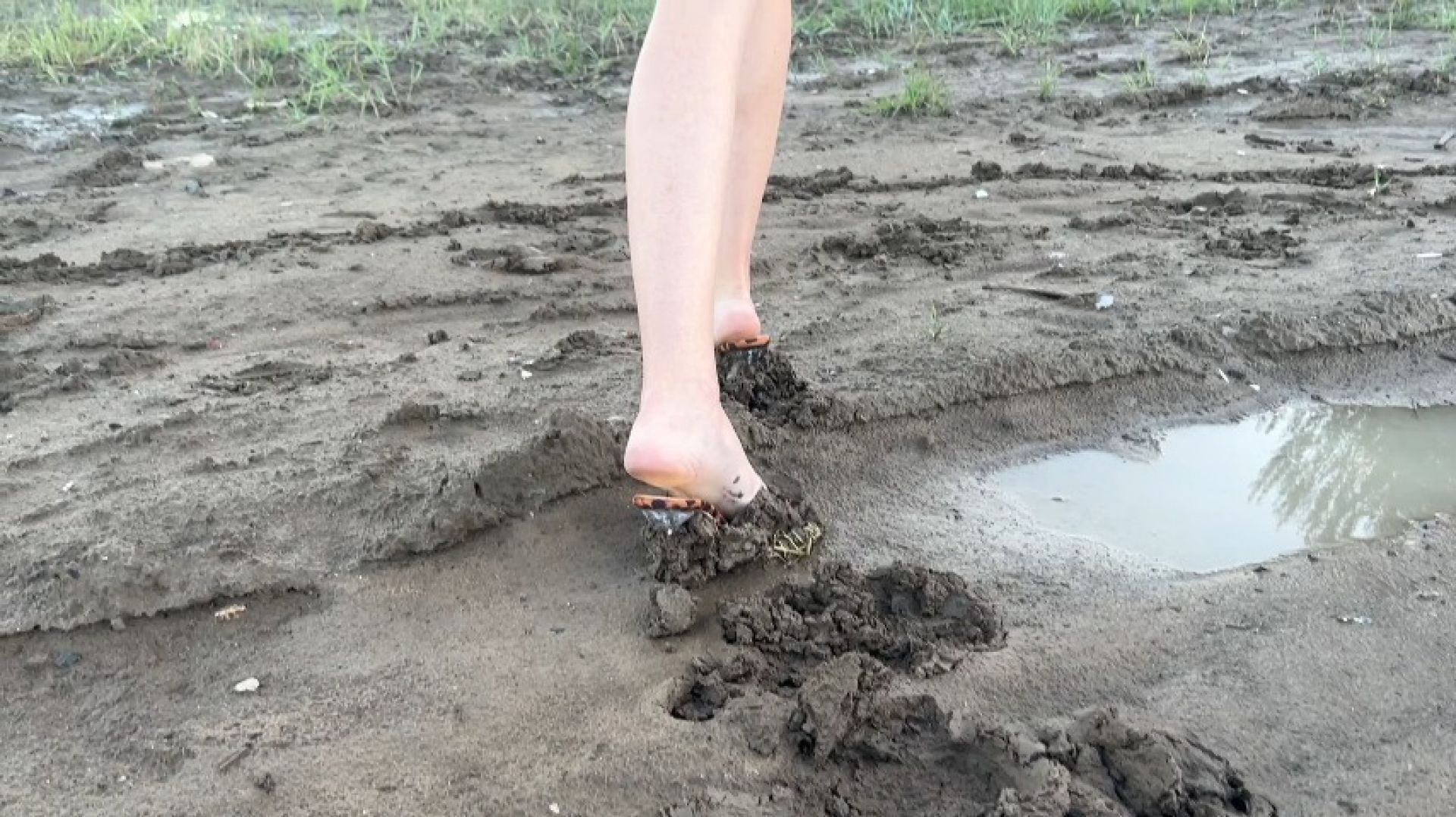 girl in high heeled mules walks through mud and often slips