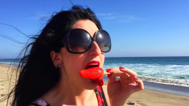 Luscious Lopez licks popsicle on beach