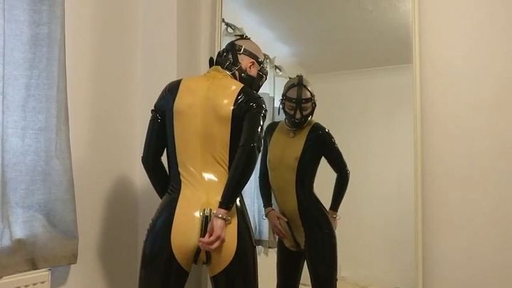 Muzzled slave in tight latex catsuit